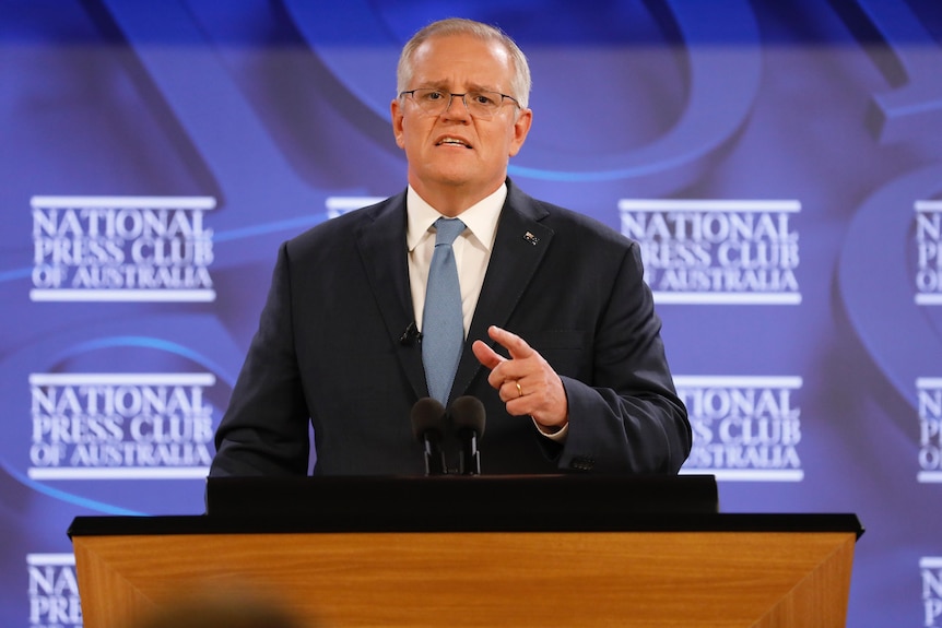 Scott Morrison wearing a suit and tie standing at a podium with the national press club logo behind him
