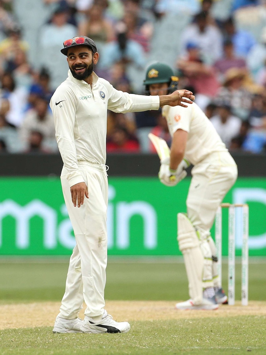 Virat Kohli smiles and points to the outfield while Tim Paine stands behind him ready to bat at the MCG