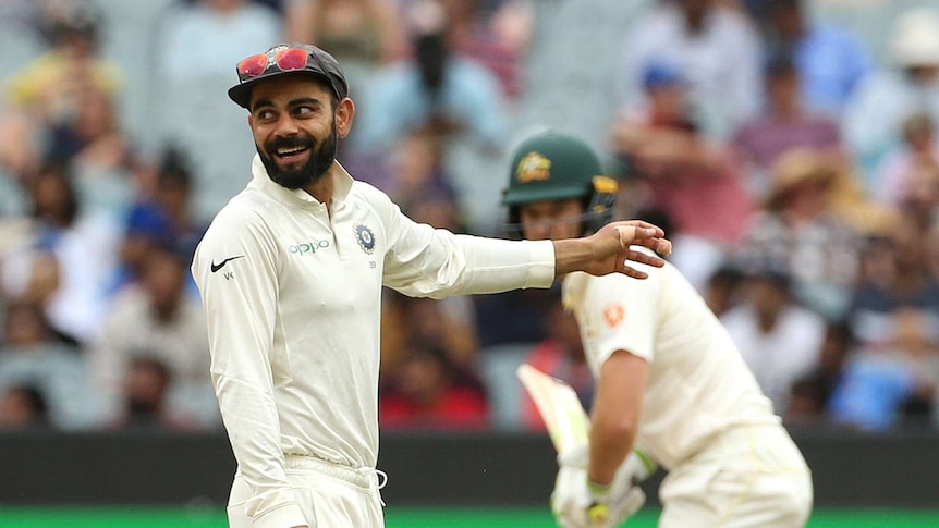 Virat Kohli smiles and points to the outfield while Tim Paine stands behind him ready to bat at the MCG