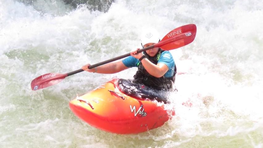 A woman navigates  in an orange kayak with an orange and black paddle
