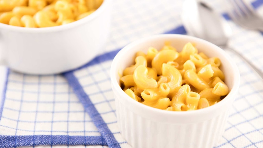 Small serving of macaroni and cheese with a larger serving dish in the background sitting on a blue kitchen towel.