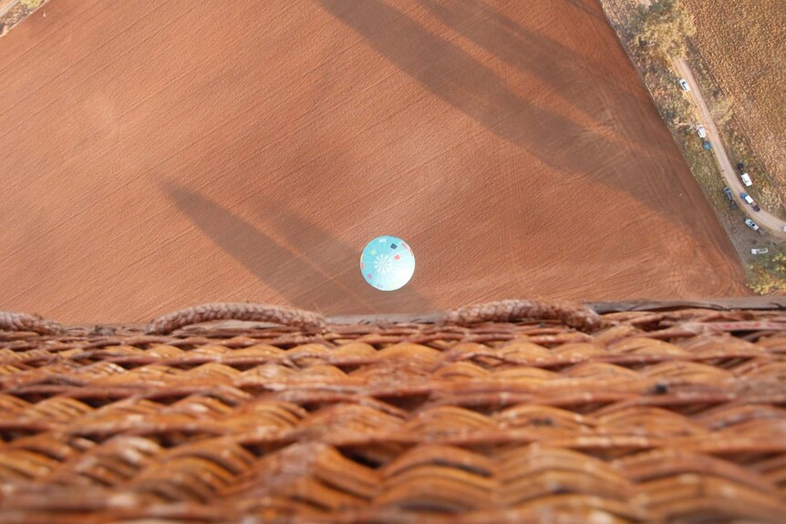 A view from a hot air balloon basket looking down onto a balloon close to the ground.