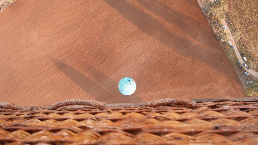 A view from a hot air balloon basket looking down onto a balloon close to the ground.