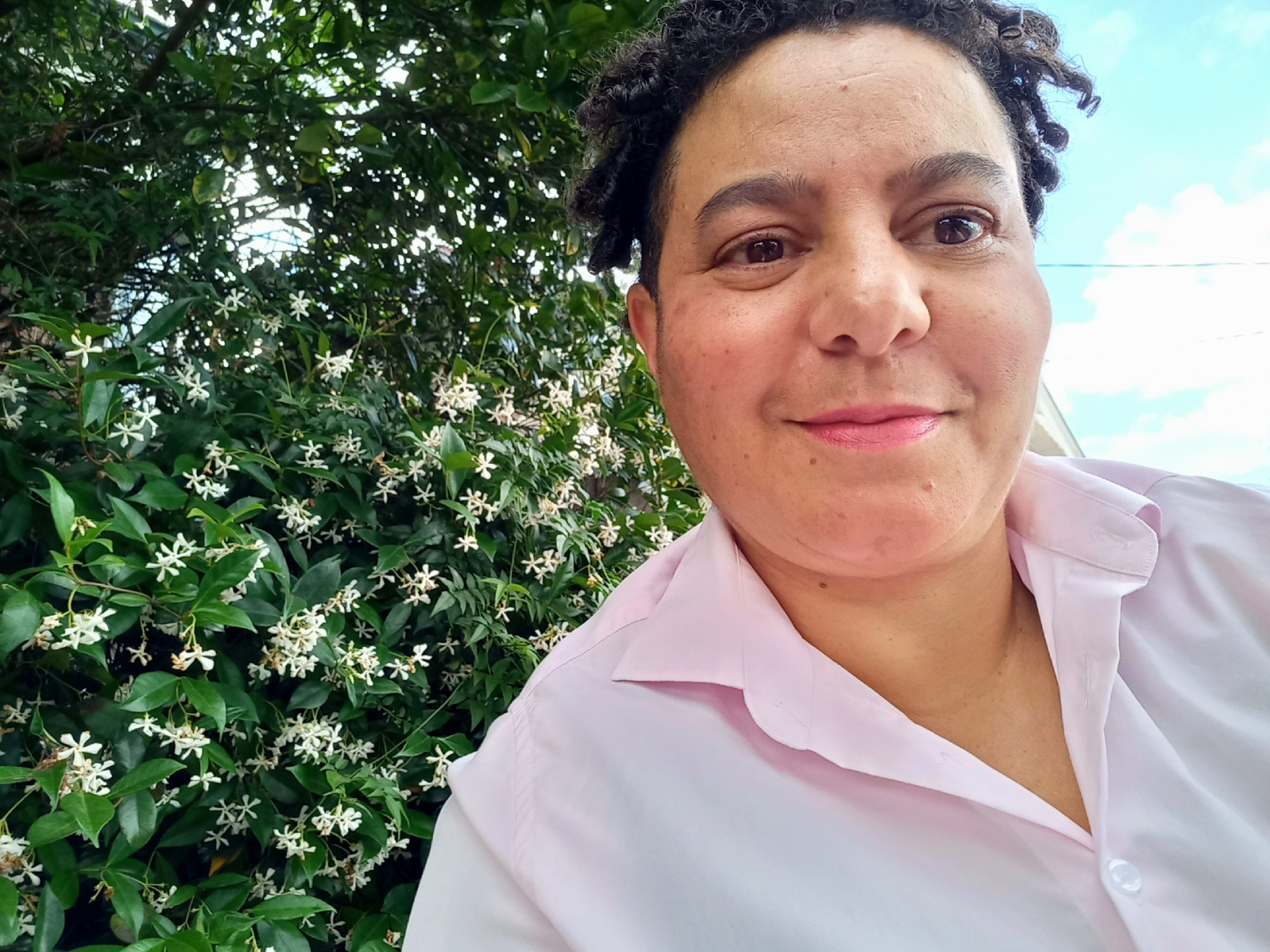 A woman smiling with a tree and flowers in the background.