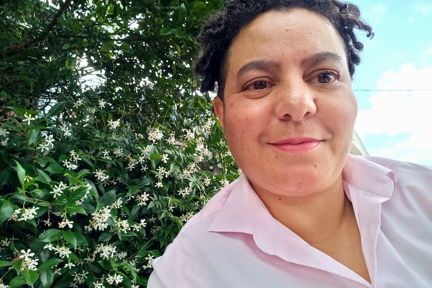 A woman smiling with a tree and flowers in the background.