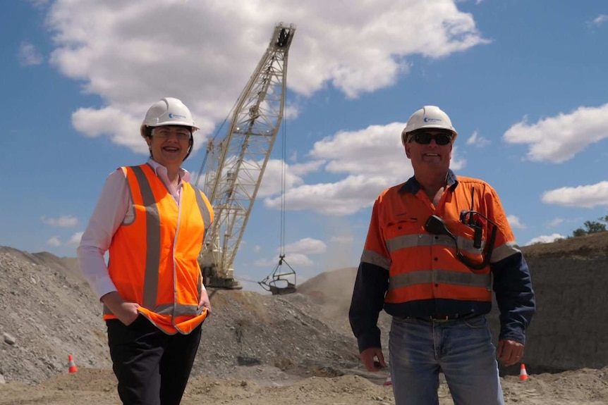 Wearing a hard hat and high-vis vest, Annastacia Palaszczuk stands in front of a crane at a mine pit.