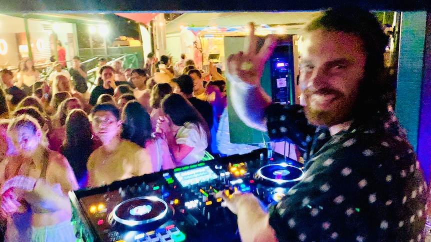 A smiling DJ performs before a packed outdoor dancefloor
