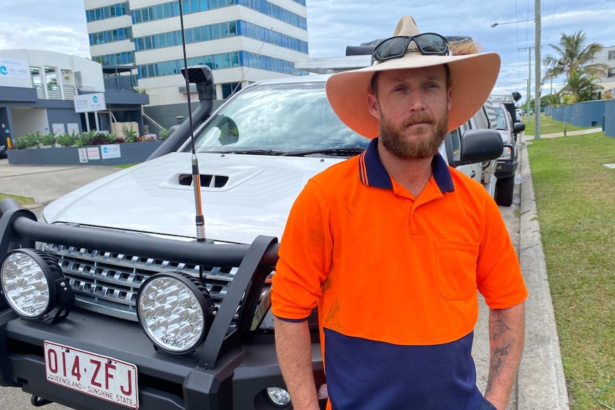 Stuart Pope in a fluroscent orange work shirt and wide brimmed hat sitting on a white vehicle