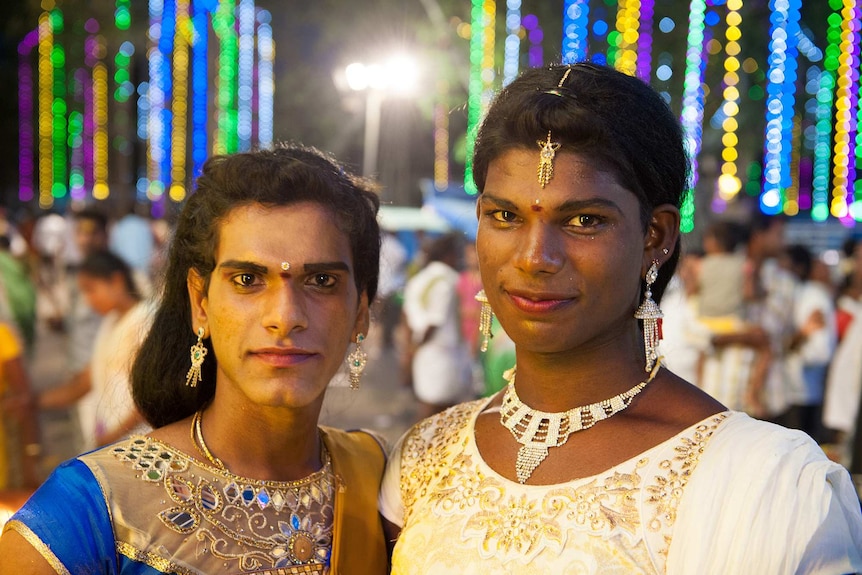 Two transgender women with festival in the background at night