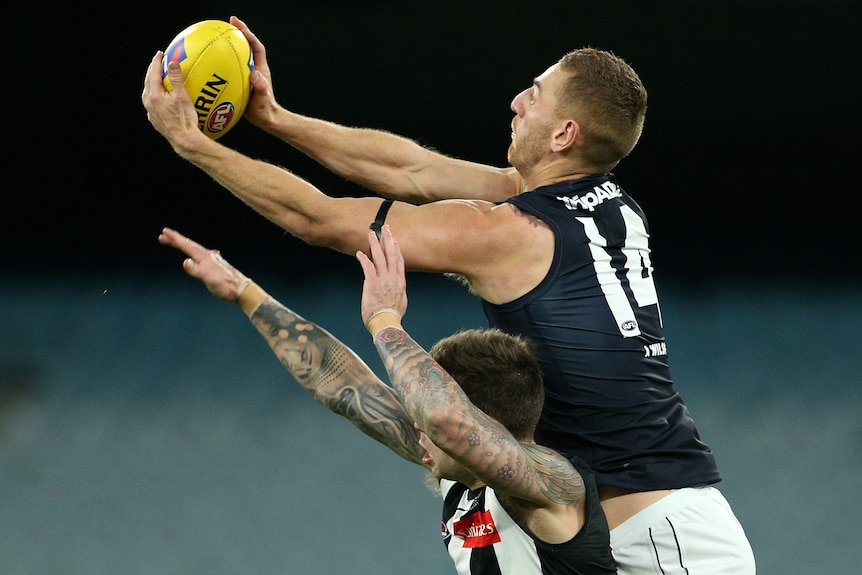 A Carlton AFL player takes a mark over the top of a Collingwood opponent.