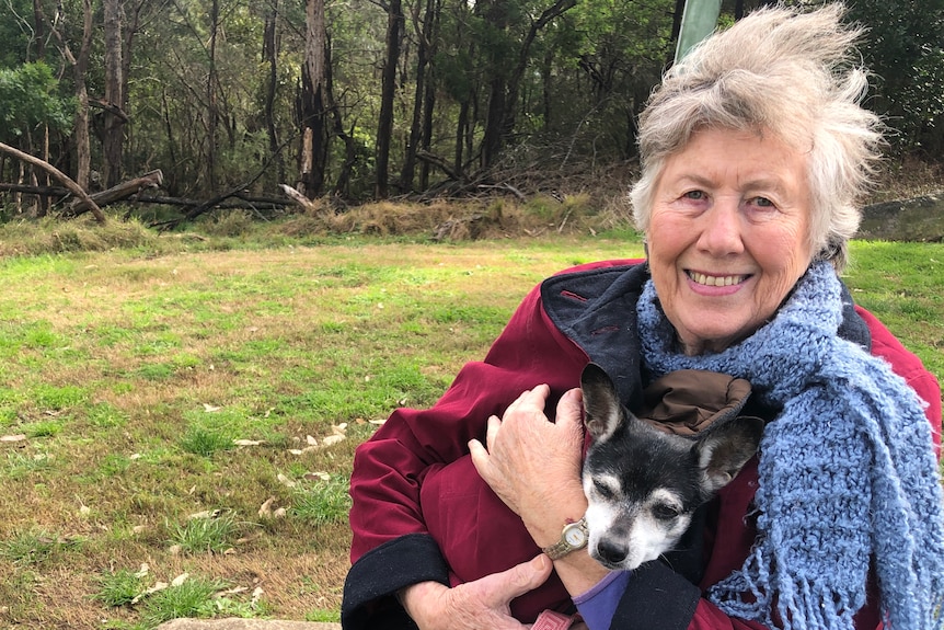 Woman holding a small dog in a park.