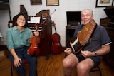 A young woman holding a violin next to an elderly man holding a harp.