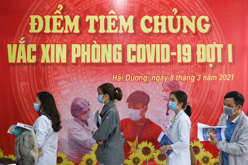 Health workers wait for their turn to be vaccinated in front of a red banner