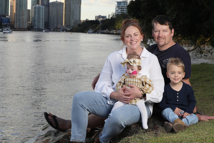 A baby girl, a little boy and their parents beside a river. 