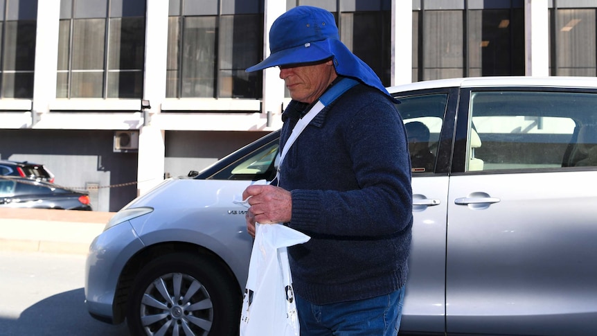 A man whose face is obscured by a large hat steps out of a car.