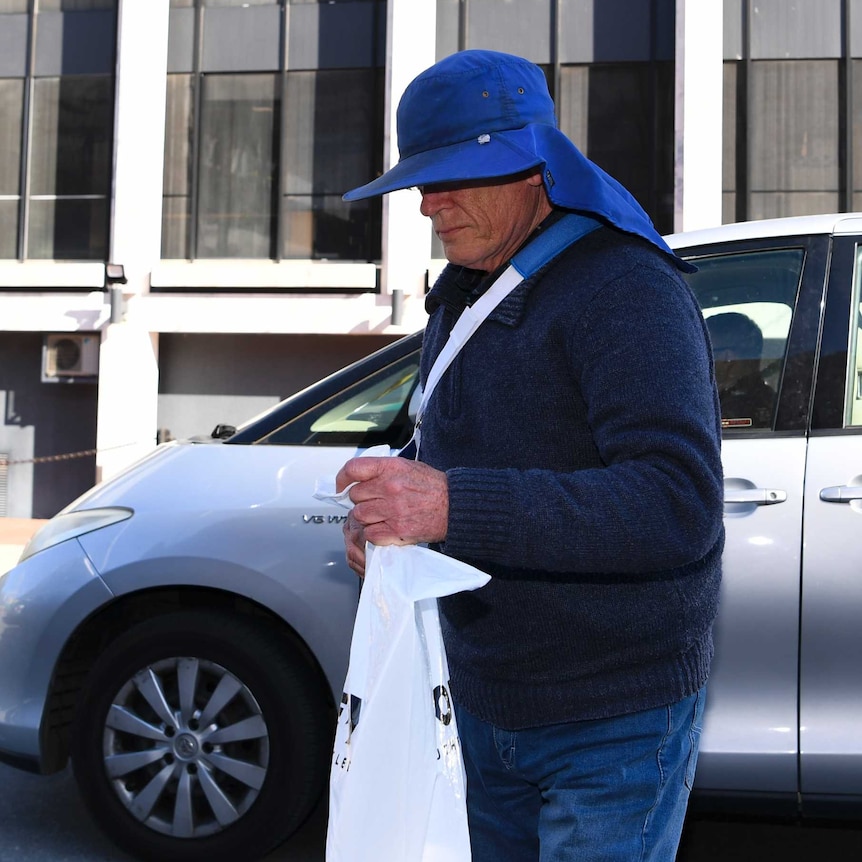 A man whose face is obscured by a large hat steps out of a car.