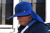 A man whose face is obscured by a large hat steps out of a car.