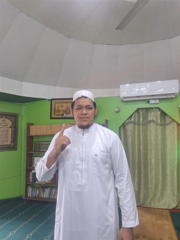 Um homem numa mesquita vestindo um thobe islâmico tradicional branco, apontando para cima com um dedo.