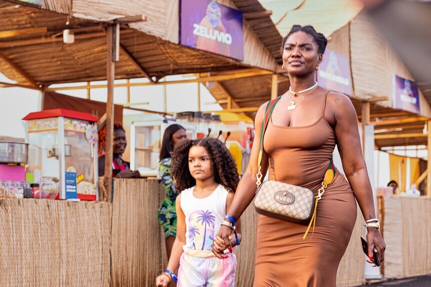 A woman and a young girl hand in hand walking past some stalls