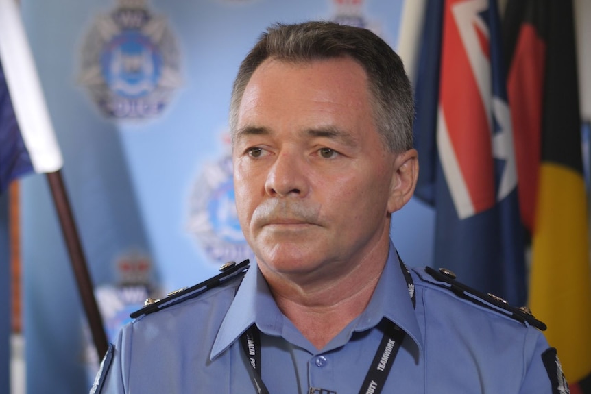 A police officer looking to the right of the camera, with the Australian flag in the background