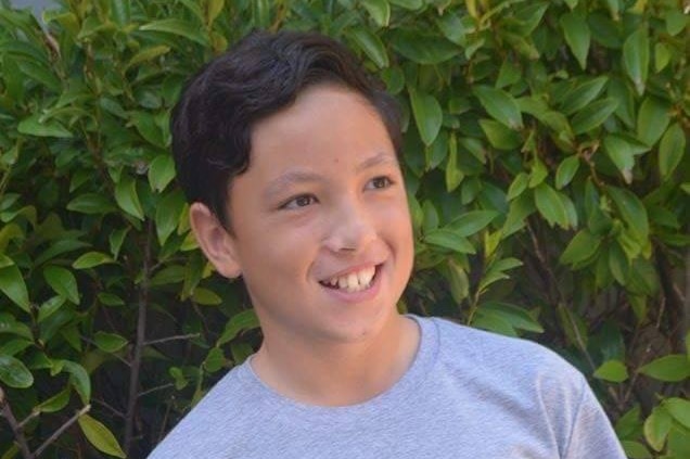 Teenager Jake Cooper stands in a grey T-shirt in front of a hedge.