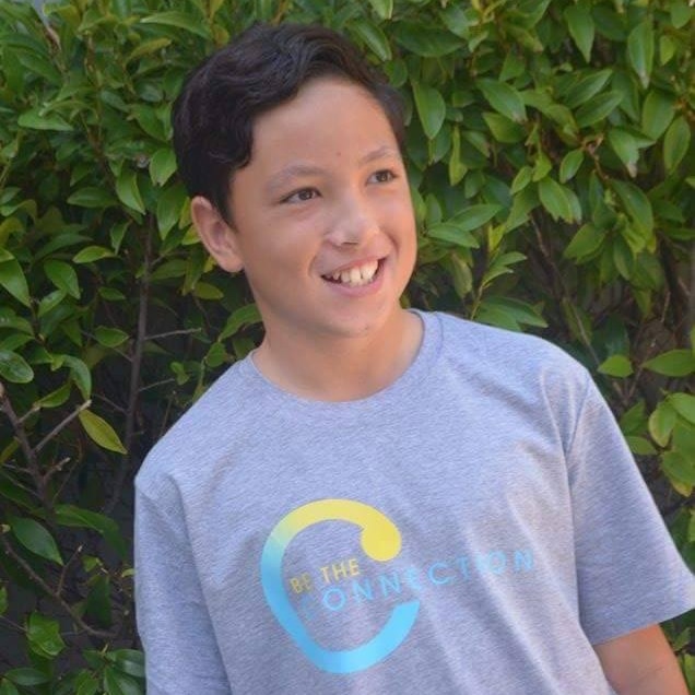 Teenager Jake Cooper stands in a grey T-shirt in front of a hedge.