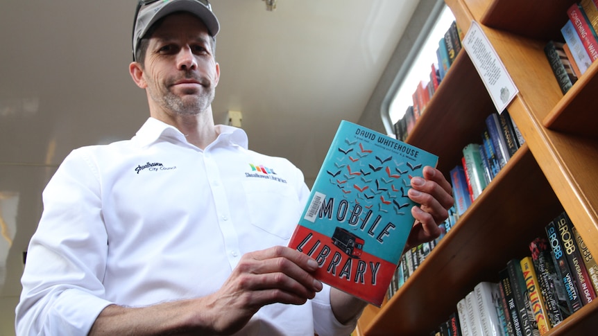 A tall man, standing in the bookmobile, holds a book titled, Mobile Library.