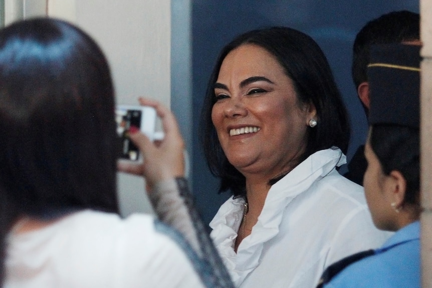 A woman smiles as bystanders take photos on their phones. 