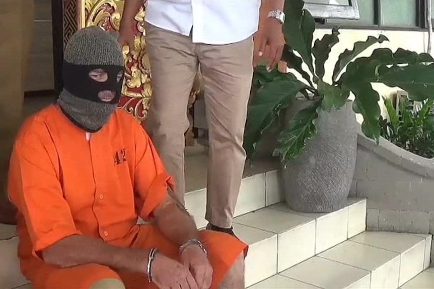 Man in orange prison outfit with black balaclava 