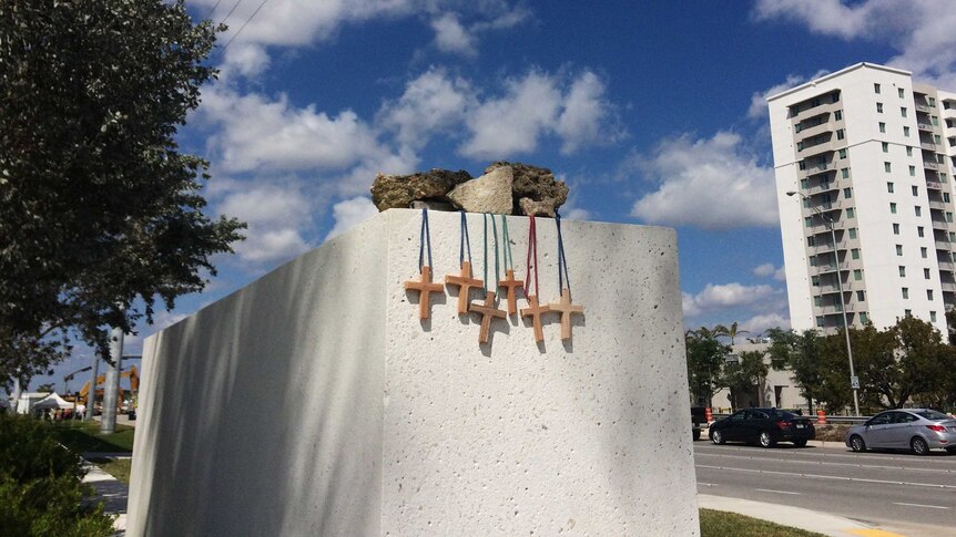Six small wooden crosses hung off a large concrete block near the side of a road.