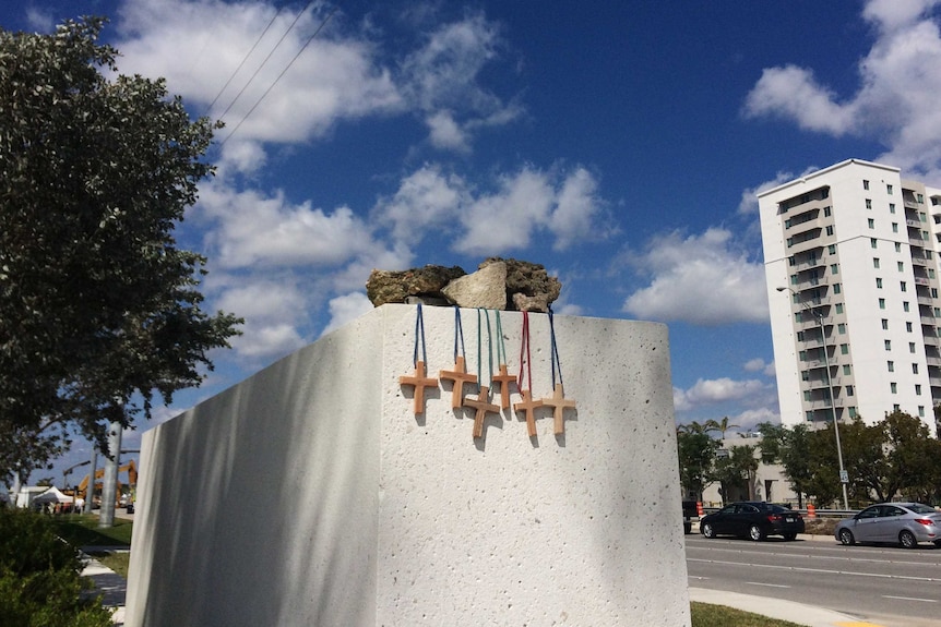 Six small wooden crosses hung off a large concrete block near the side of a road.
