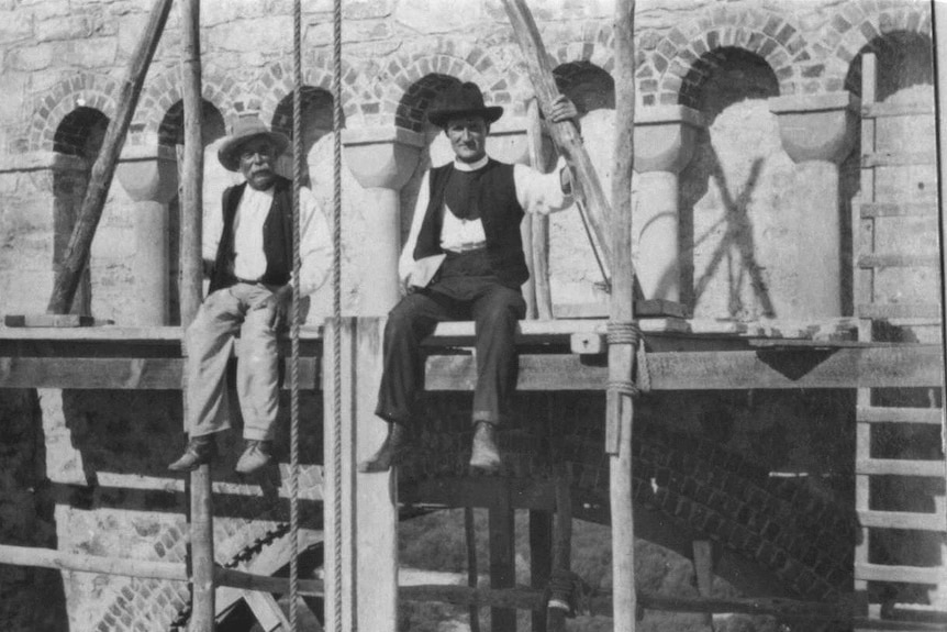 Monsignor John Hawes and a worker sit on a platform