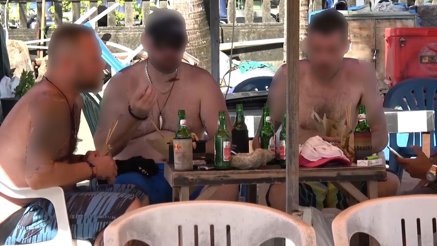 Three tourists eating satay on a beach in Bali