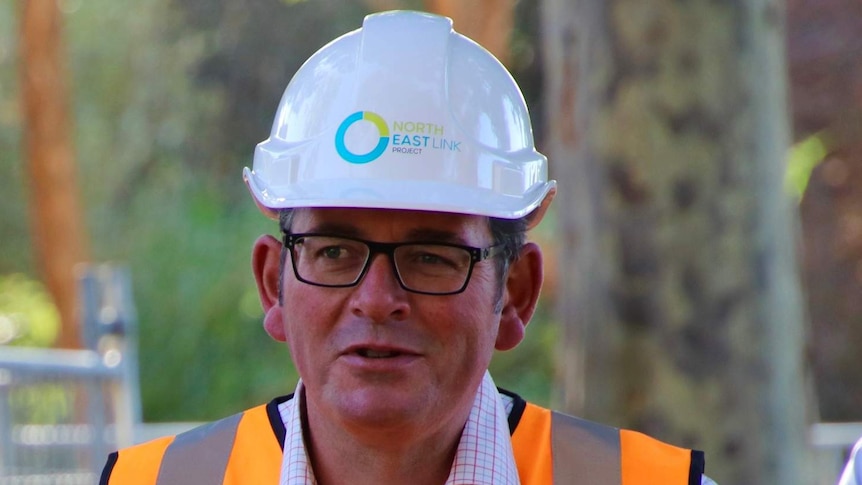 Premier Daniel Andrews wears a hard hat and high-vis vest at a press conference.