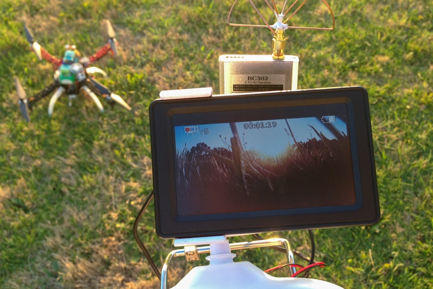 A drone rests on the grass with remote control and camera monitor.