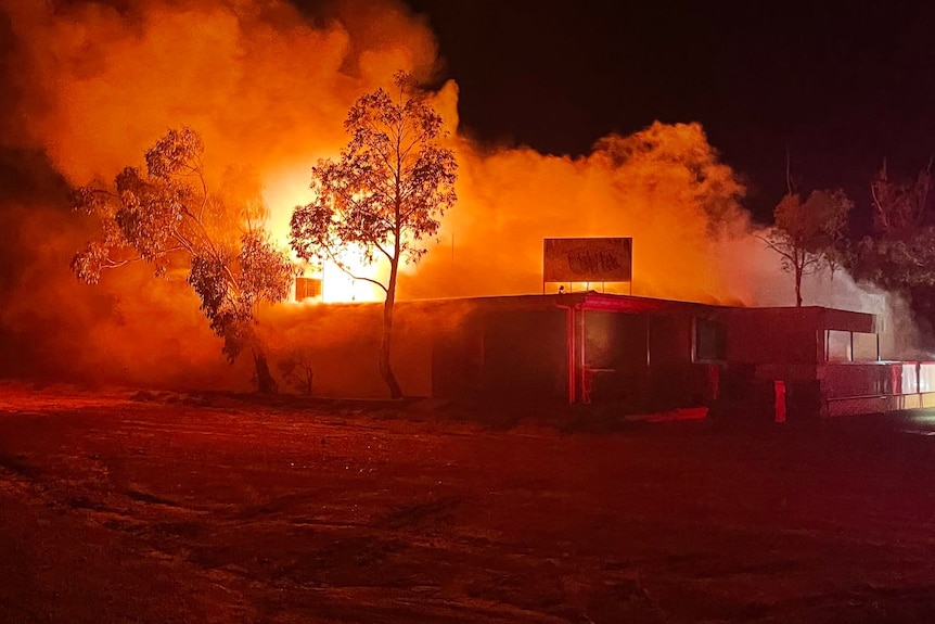 The Andamooka hotel on fire with flames and smoke coming from the roof with trees on the side