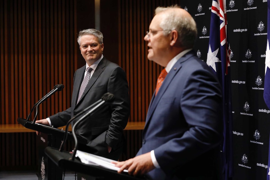 Mathias Cormann looks at Scott Morrison as they address the press from lecterns