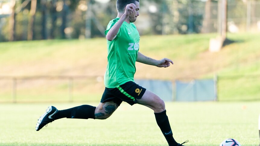 A man in a green shirt sprints across a soccer pitch with a soccer ball