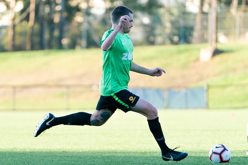 A man in a green shirt sprints across a soccer pitch with a soccer ball