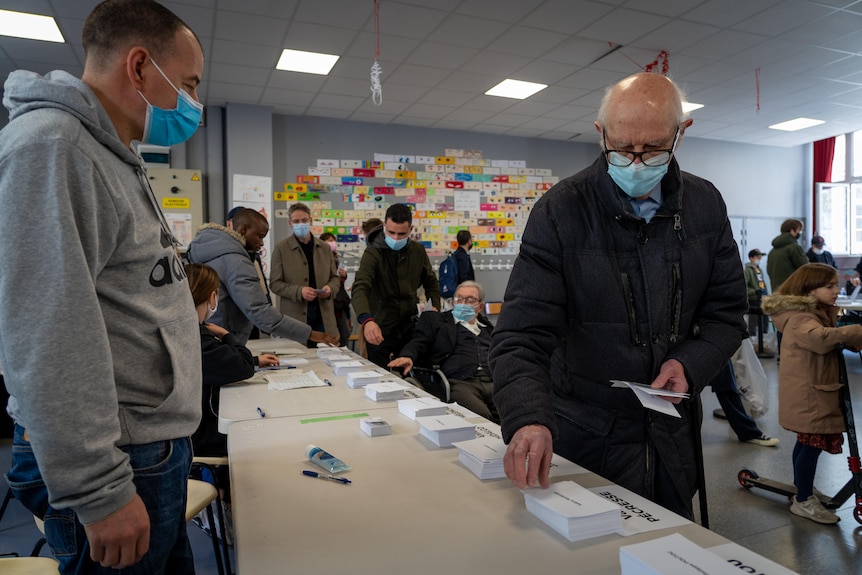 An elderly man in a mask picks up a voting card at a polling station in France.