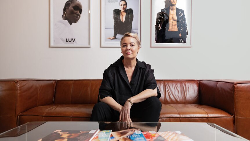 Woman wearing a black outfit sits on a brown leather couch. Magazines are in front of her on a coffee table