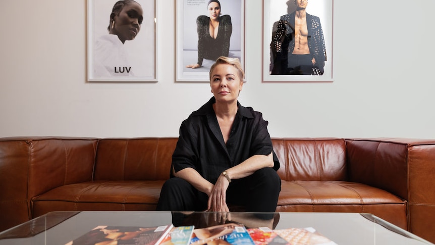 Woman wearing a black outfit sits on a brown leather couch. Magazines are in front of her on a coffee table