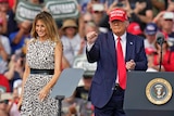 A woman in a leopard pattern dress stands next to a man wearing a suit with a red tie wearing a Make America Great Again cap