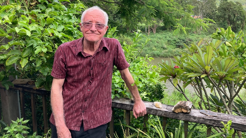 Man wearing a red shirt looking at camera, standing on a timber deck with a river in the background