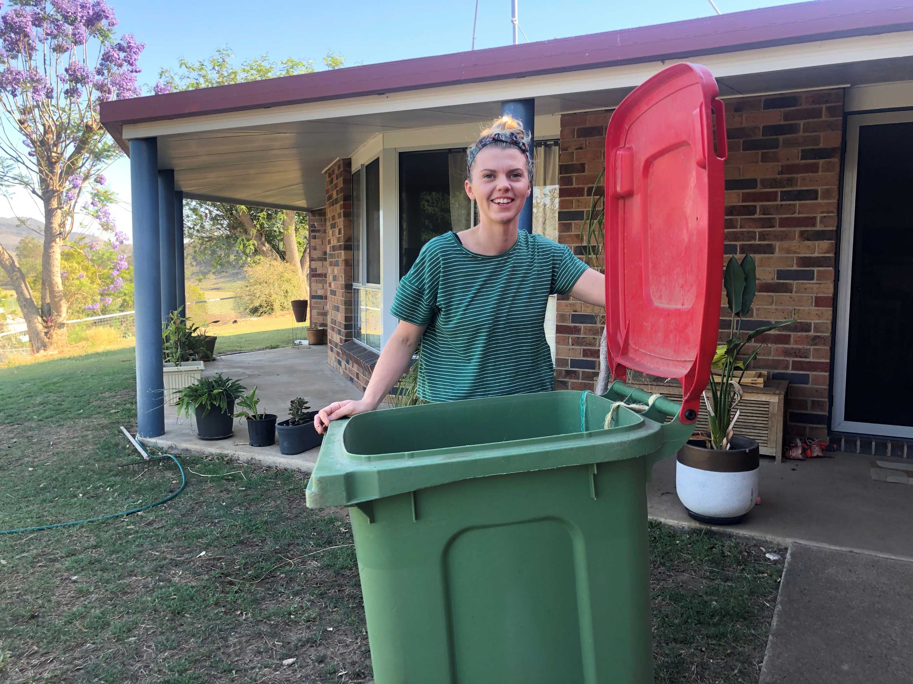 Journalist Elly Bradfield stands behind her wheelie bin holding the red lid open and smiling