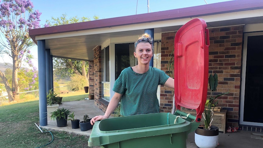 Journalist Elly Bradfield stands behind her wheelie bin holding the red lid open and smiling