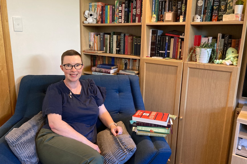 Amy Heap sits in a large blue chair, behind her are shelves of books, with various nicknacks around.