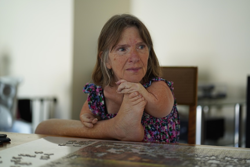 Trish Jackson with her head resting on her hand, which is on her foot, looking into distance