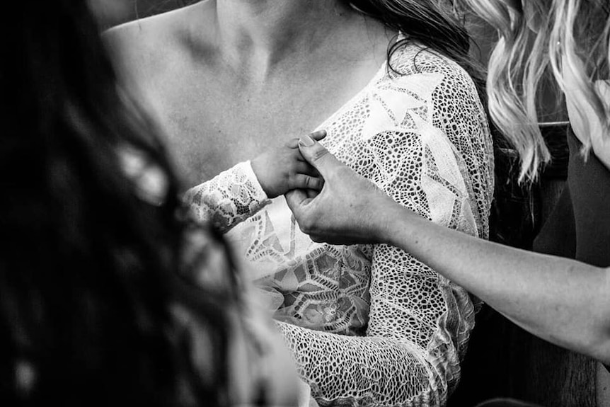 A black and white photo with a woman holding a baby reaching out to another woman