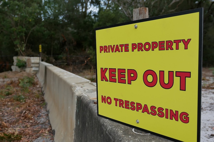 A concrete barrier with a large yellow sign on top of it reading 'private property, keep out, no trespassing'.